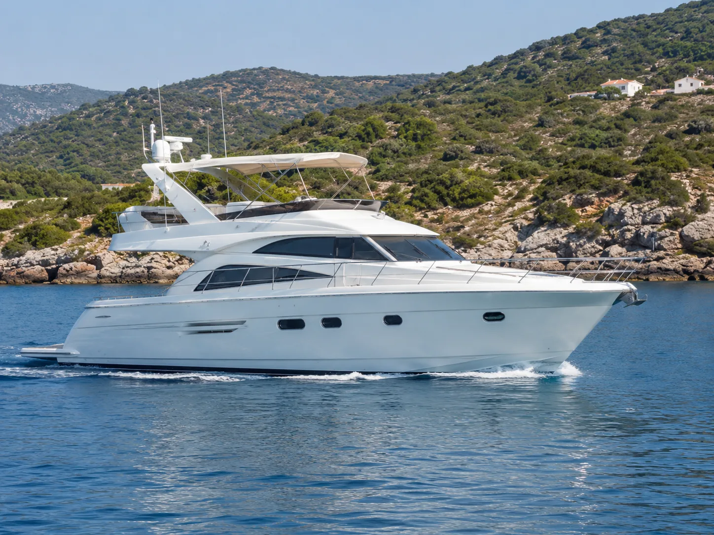 Weiße Flybridge-Motoryacht in Fahrt vor einer felsigen griechischen Küste